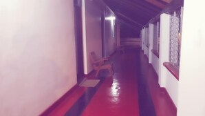 A narrow hallway with a red and black striped floor, a wooden chair, and a metal gate on the right. - Delight Guest House And Restaurant (Pasikuda)