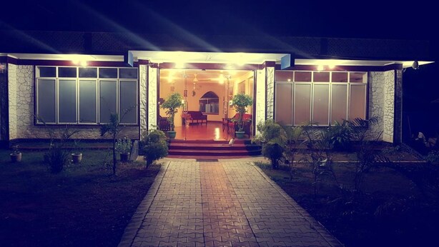 A modern house with a paved driveway leading to a front door, flanked by potted plants and a small garden area. - Delight Guest House And Restaurant (Pasikuda)