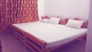 A single-bed room with a wooden headboard, white bedding, and a patterned curtain. - Delight Guest House And Restaurant (Pasikuda)