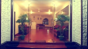 A hotel lobby with a red carpet, two potted plants, a reception desk, and a seating area with red chairs. - Delight Guest House And Restaurant (Pasikuda)