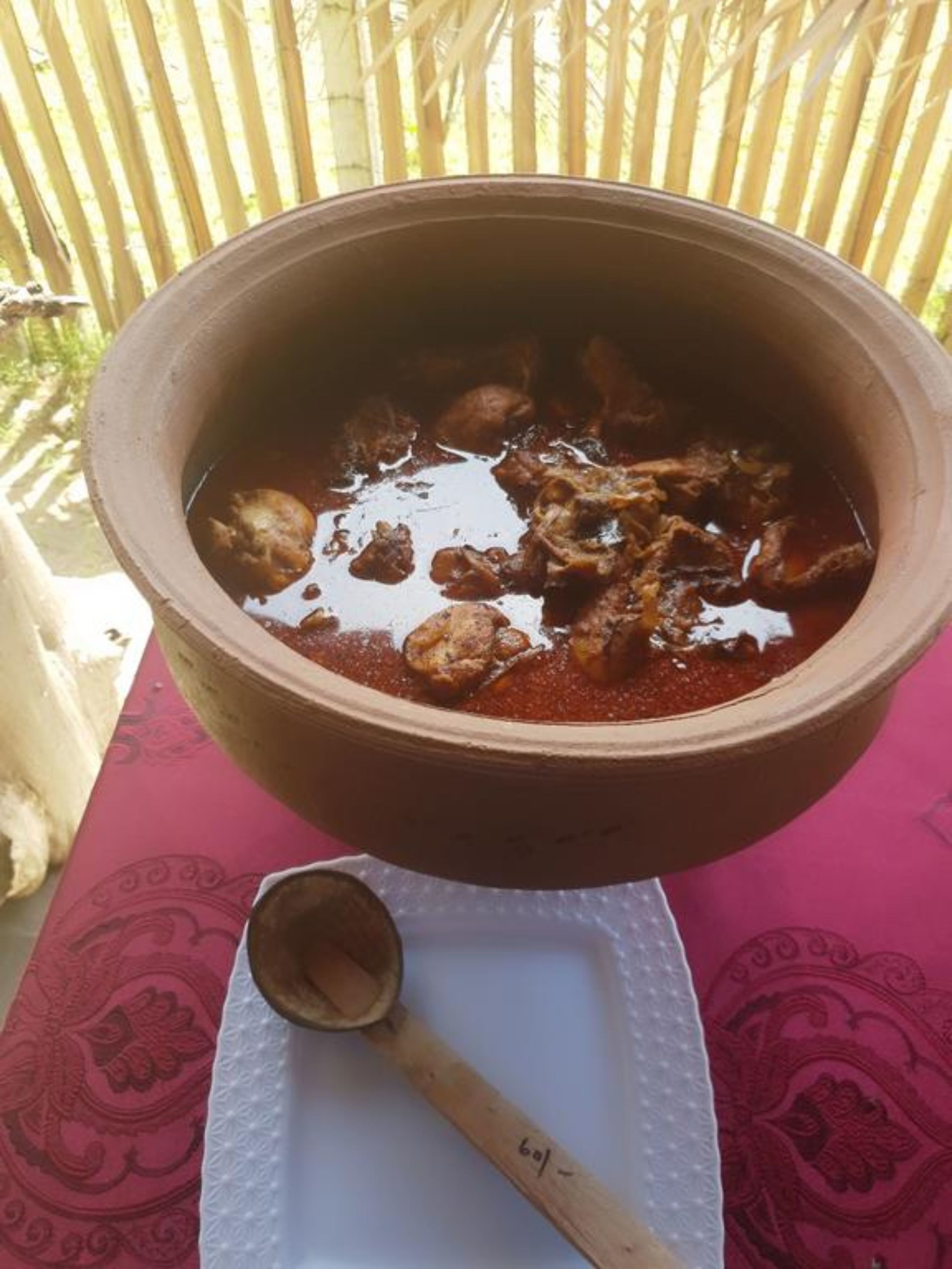 Una olla de barro grande llena de estofado, sobre una mesa con mantel estampado.