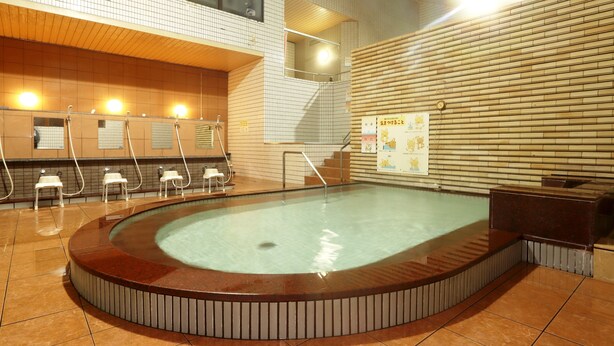 A public bath area with a central pool, multiple shower stations, and a tiled wall with informational posters. - Tuji Wakuwaku Land Minshuku Chaya (Uozu)