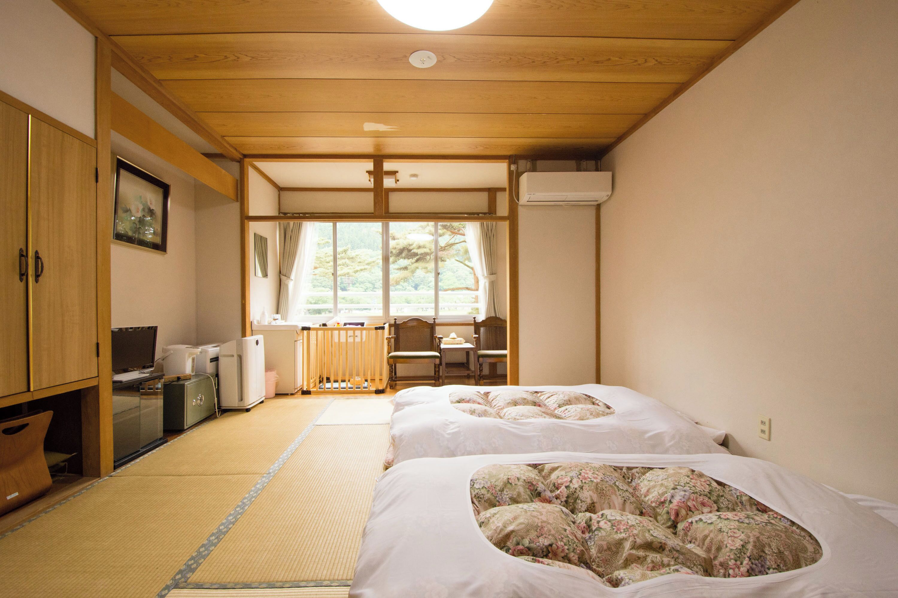 A traditional Japanese room with tatami flooring, a futon bed, a desk, and a television.