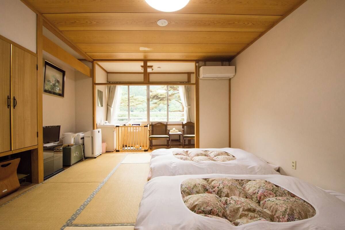 Une pièce de style japonais traditionnel, avec un sol recouvert de tatamis, un futon servant de lit, un bureau et un téléviseur.
