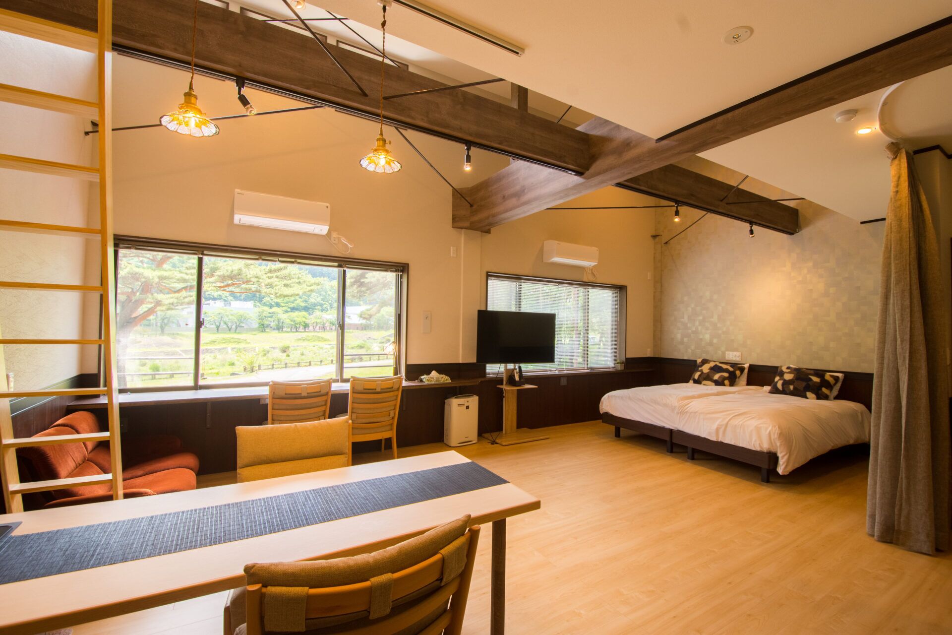 A room with a bed, a TV, a desk, and a window with a view of trees.