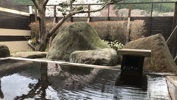 A tranquil indoor water feature with a stone basin, surrounded by rocks and a wooden bench.