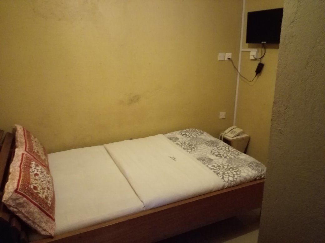 A single bed with a patterned blanket, a bedside telephone, and a wall-mounted TV.