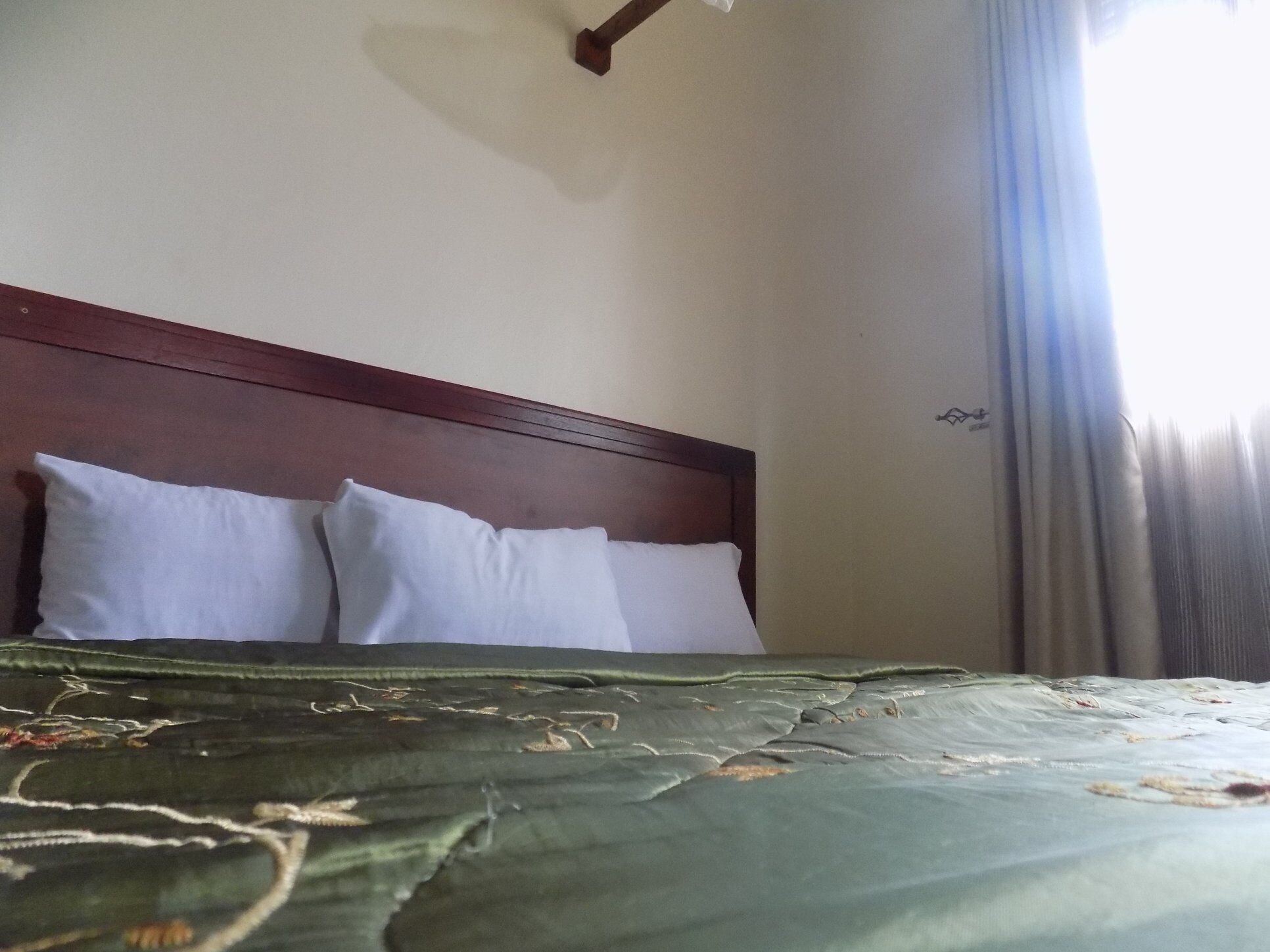 Una cama con cabecera de madera, dos almohadas blancas y una colcha verde con motivos florales.
