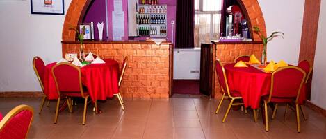 A restaurant with red tables and chairs, a brick counter, and a purple wall.
