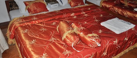 Habitació d'hotel amb un llit gran, cobros floral vermell i daurat, almoinos blancs i una manta blanca.