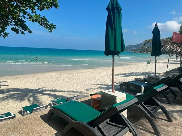 Una playa con sillas de descanso y sombrillas, cielo despejado y el océano al fondo.