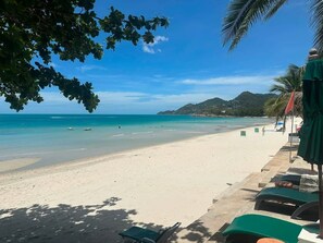 A beach with clear turquoise water, a sandy shore, and a view of a hilly landscape in the distance. - Chaweng Bliss Bungalow (Koh Samui)