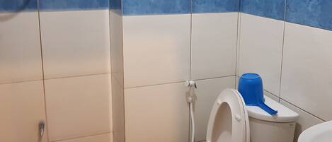 Un baño con un inodoro, un bidé, un cubo azul y un bote de basura verde.