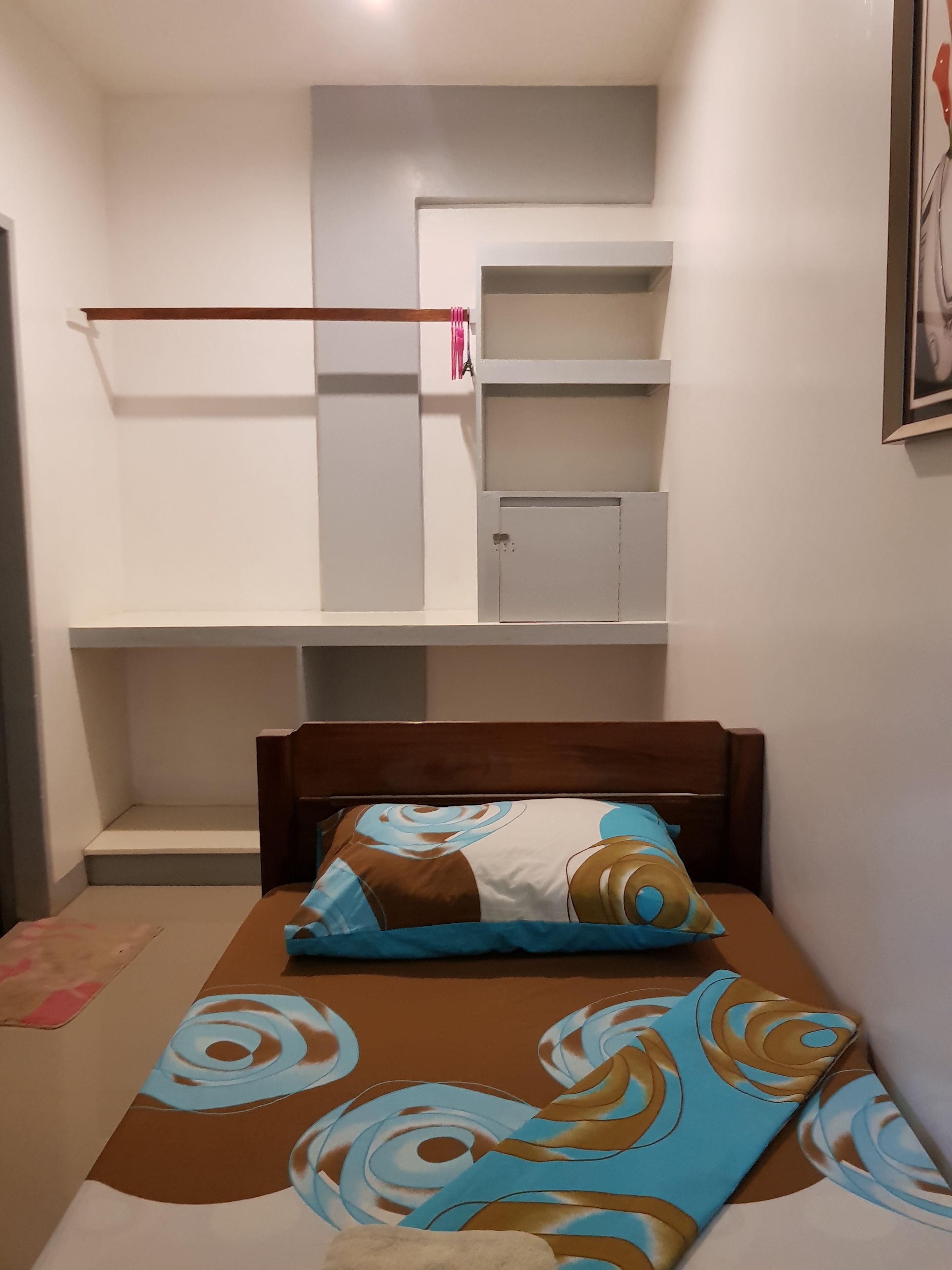 Un dormitorio con cama, cabecera de madera, estantería empotrada y una puerta.