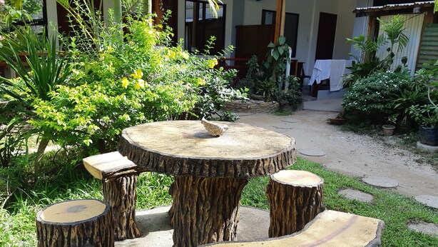 A round wooden table with four matching stools, surrounded by lush greenery and a gravel path. - Hidden Garden Pension (El Nido)