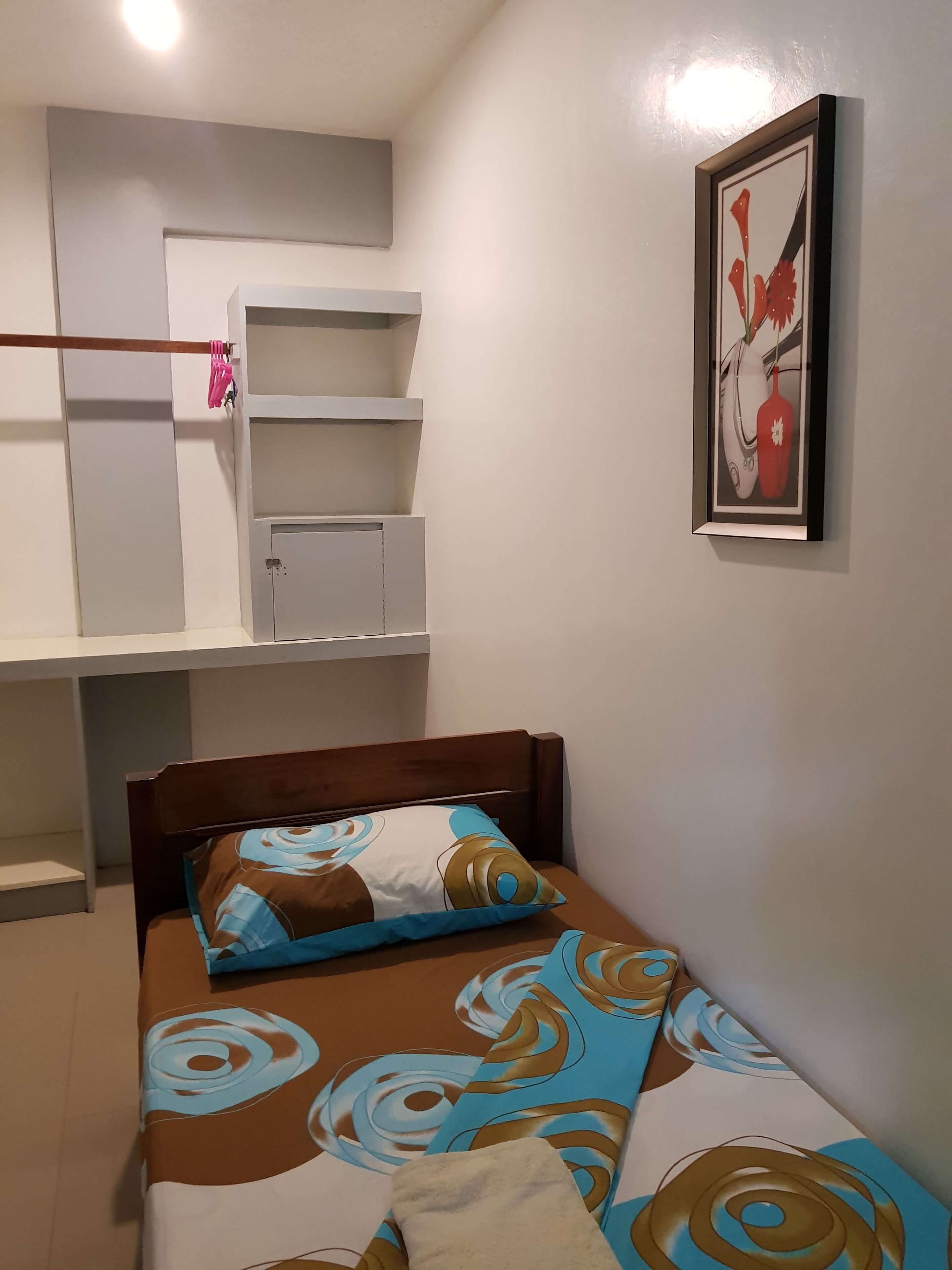 Une petite chambre à coucher, bien rangée, avec un lit simple, une armoire et une œuvre d’art encadrée accrochée au mur.