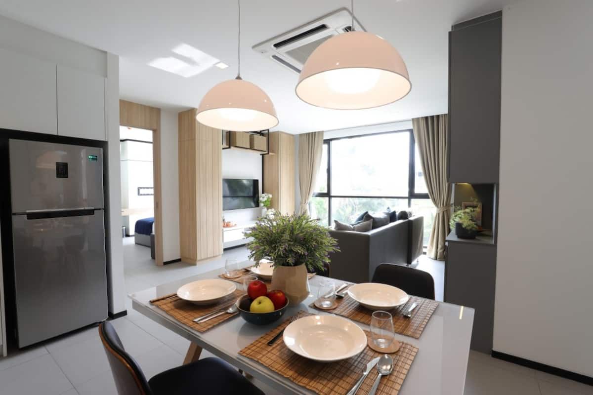 A modern kitchen with a built-in refrigerator, a dining table set with plates, cutlery, and a bowl of fruit.