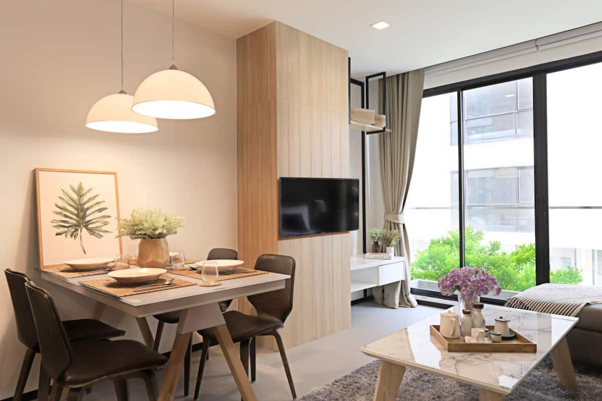 A modern living room with a large window, a flat-screen TV, and a dining area with a table set for four.