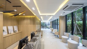 A modern reception area with a marble counter, wooden paneling, and a seating area with white chairs. - Alix Bangkok Hotel (Bangkok)
