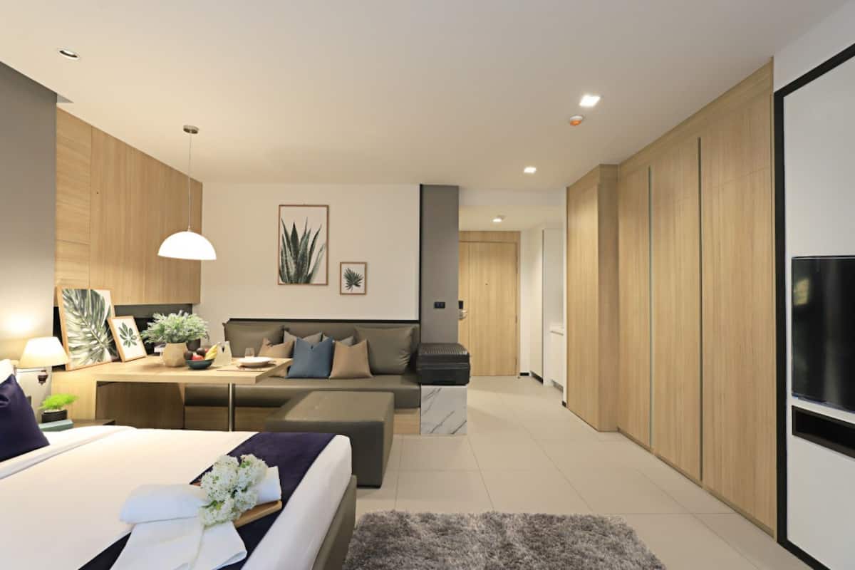 A modern hotel room with a bed, a sofa, a desk, and a TV.