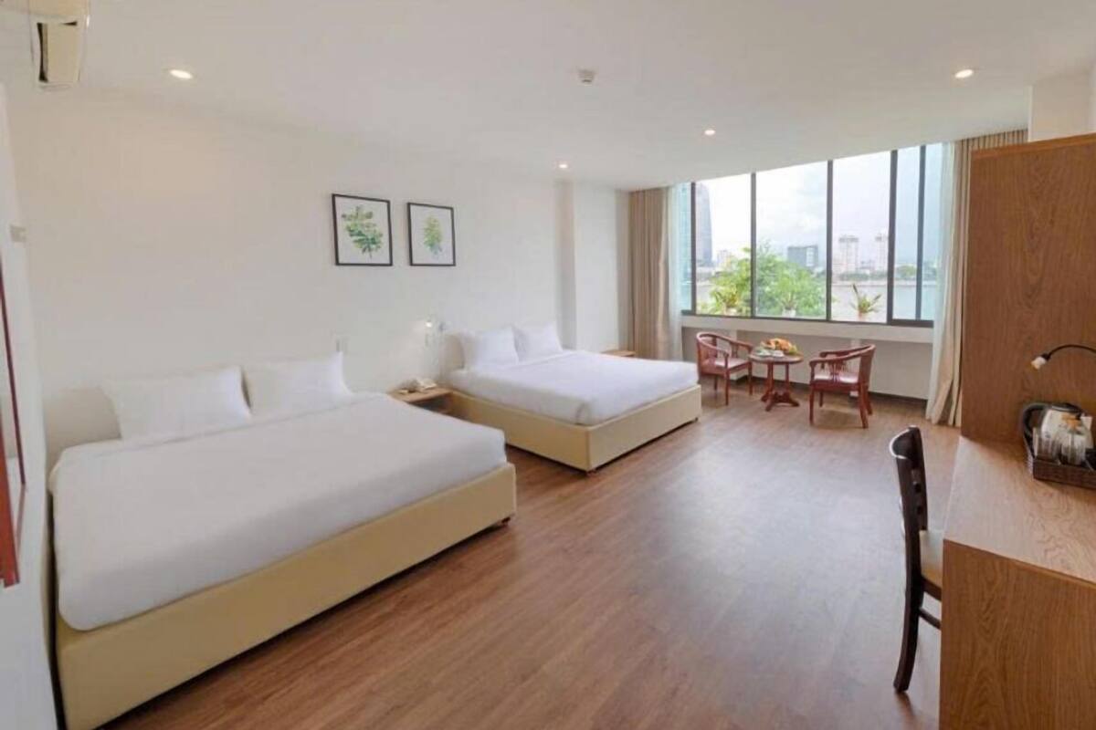 A hotel room with two beds, a dining area, and a large window offering a city view.