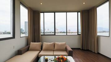 Habitación de hotel moderna con sofá, una mesa de centro de vidrio y vista del paisaje urbano a través de amplios ventanales.