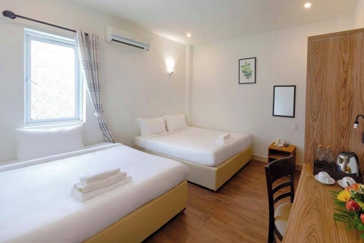 A hotel room with two beds, a wooden desk, a chair, a small table with a phone, and a window with curtains.