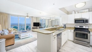Una cocina moderna con una isla central, electrodomésticos de acero inoxidable y un amplio ventanal con vista al océano.