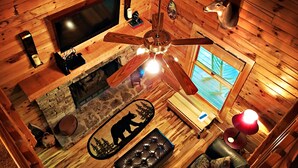 Interno di una baita con televisione, ventilatore a soffitto, camino in pietra e un'opera d'arte raffigurante la sagoma di un orso.