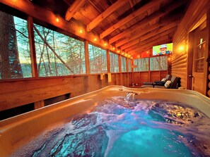 Una cabaña de madera con jacuzzi, ventanas amplias y televisor.