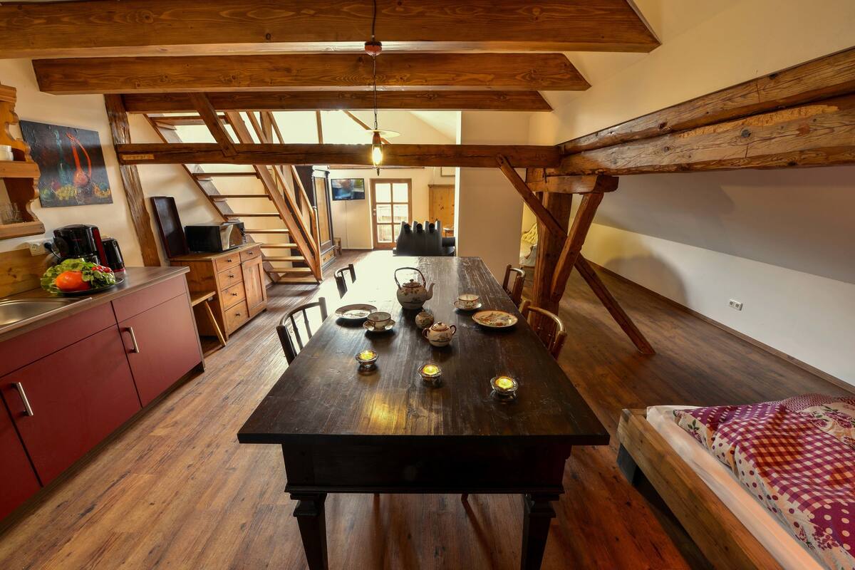 Eine rustikale Küche mit Holzbalken, einem mit Kerzen gedeckten Esstisch und einem gemütlichen Bett mit einem gemusterten Überwurf.