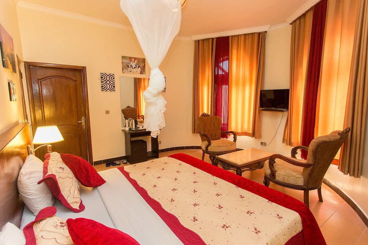 Habitación de hotel con cama, escritorio, silla, televisor y cortinas.