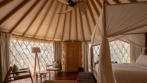 Una carpa espaciosa con una cama, una silla, una mesa y una lámpara.