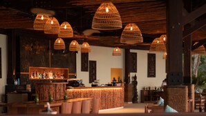 A restaurant with wooden furniture, woven pendant lights, and a stone wall.
