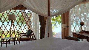 Un dormitorio con una cama, una silla, un escritorio y vistas al exterior a través de una ventana con celosía.