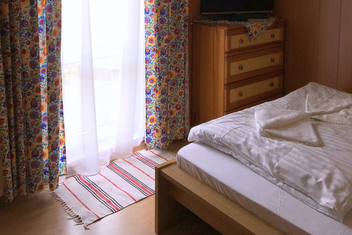 Un dormitorio con cama, cómoda de madera, televisor y cortinas.