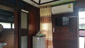 A compact room with wooden walls, a small refrigerator, a television mounted on the wall, and a window with a curtain. - Sarocha Resort Rayong (Rayong)