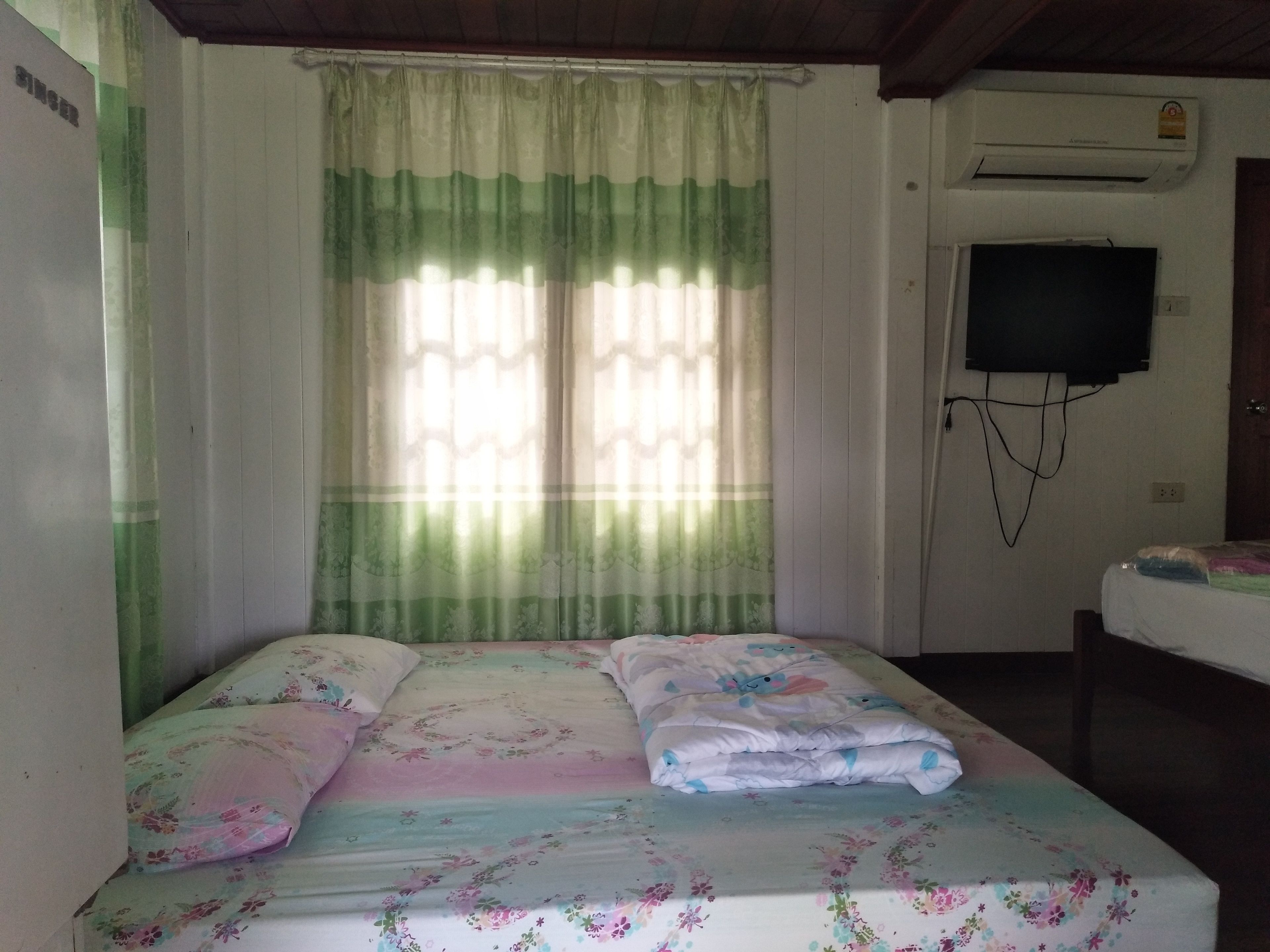 A room with a bed, a television mounted on the wall, and a window with curtains.