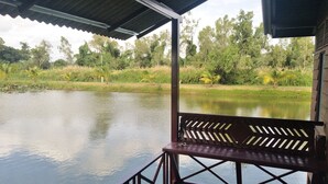 A wooden deck with a bench overlooking a calm body of water, surrounded by lush greenery and trees. - Sarocha Resort Rayong (Rayong)