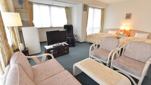 A hotel room with a sofa, two armchairs, a small table, a TV, a mini-fridge, a lamp, and a nightstand with a lamp. - Hotel Garden Hills (Kumejima)