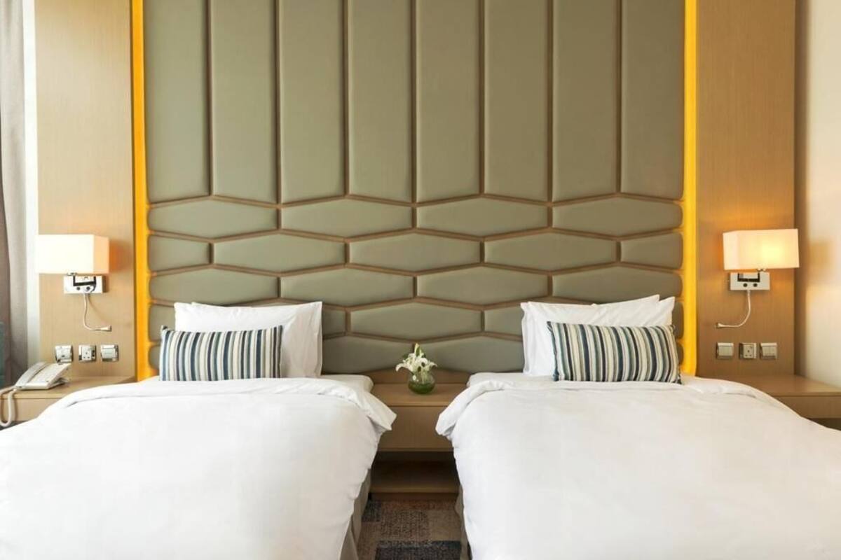 A hotel room with two beds, a geometric headboard, bedside lamps, a phone, and a vase with flowers.