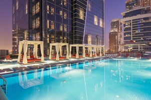 Una piscina con sillones de playa y sombrillas, rodeada de edificios altos.