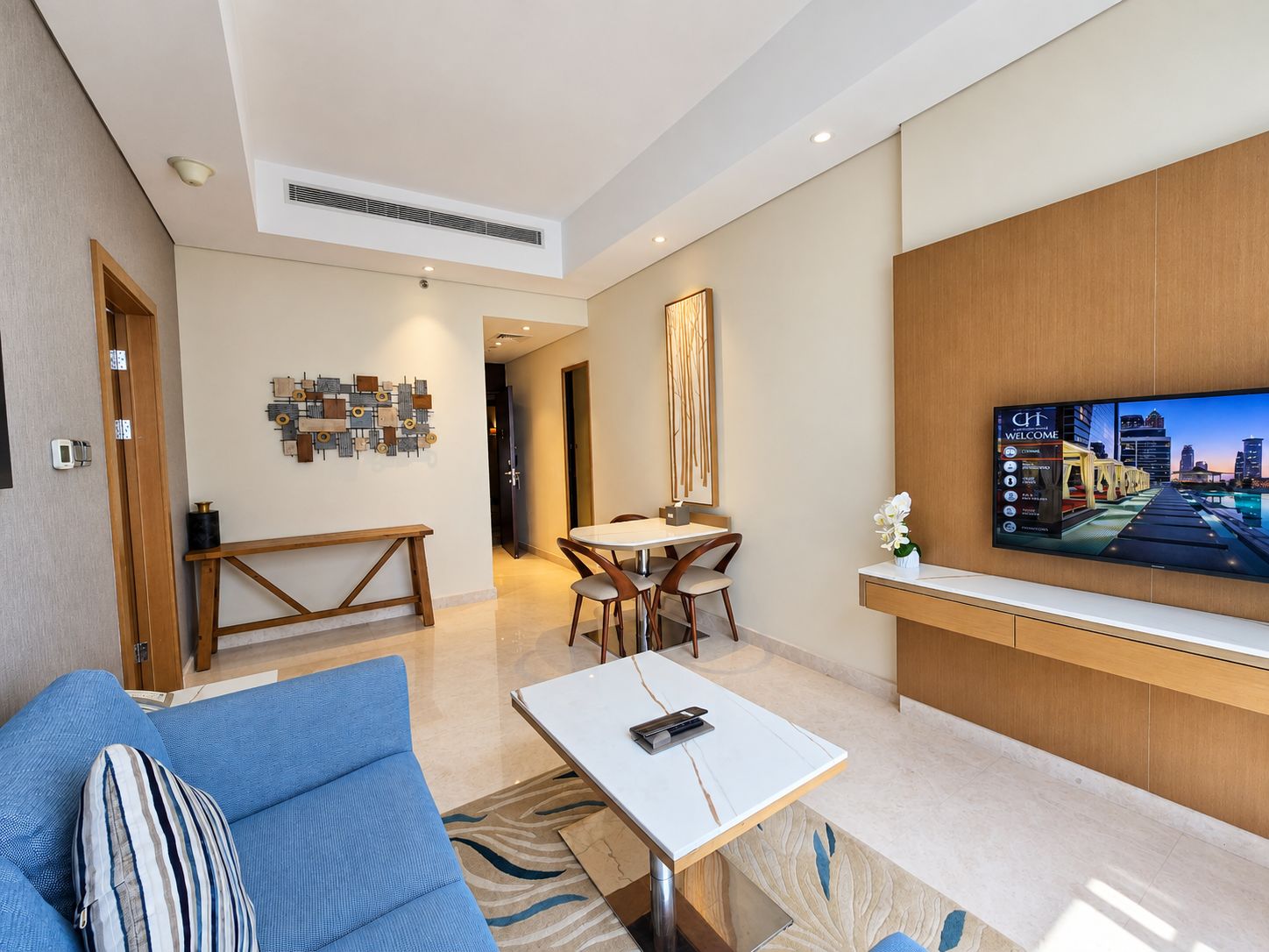 A modern living room with a sofa, coffee table, TV, and a dining area with chairs and a table.