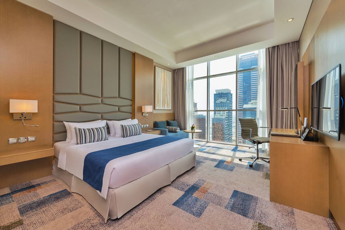 A modern hotel room with a large bed, a desk, a chair, and a TV.