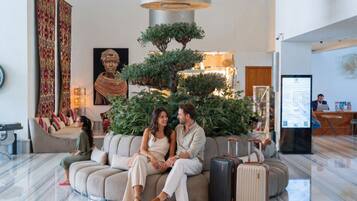 A modern lobby with a seating area, a reception desk, and a large plant centerpiece.