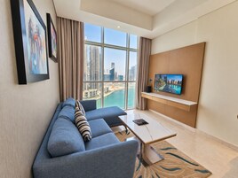 A modern hotel room with a large window, a sofa, a coffee table, and a mounted TV.