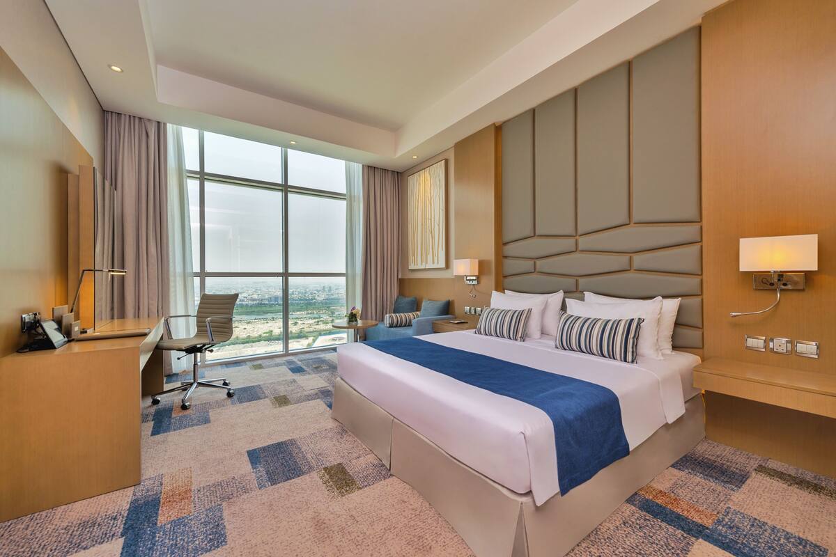 A modern hotel room with a large bed, a desk, and a view of the city.