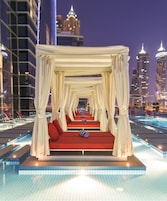 A luxurious outdoor pool area with a canopy bed, red cushions, and a view of the city skyline at night.
