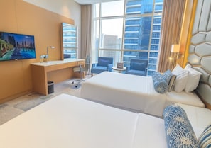 A hotel room with two beds, a desk, a chair, a TV, and a large window with a city view.