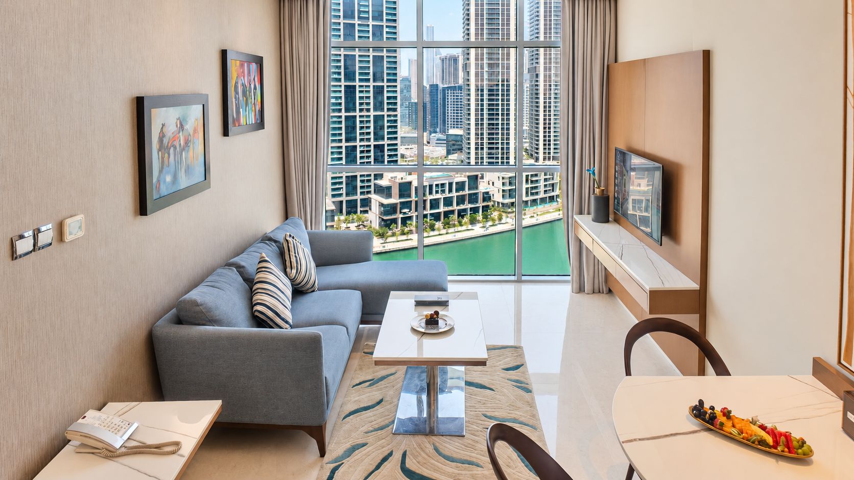 A modern living room with a sofa, a dining table, and a view of a cityscape through large windows.